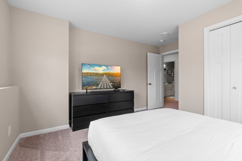 Cozy bedroom with a neutral color palette, a flat-screen TV, and a black dresser.