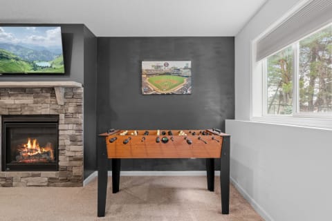 Foosball table in a game room with a stone fireplace and a TV showing a landscape.