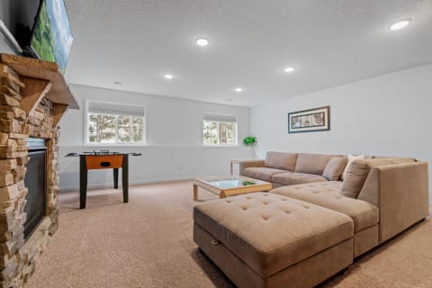 A comfortable living room featuring a sectional sofa, foosball table, and stone fireplace.