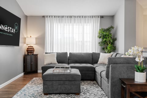 A modern living room with a gray sectional sofa, an area rug, and decorative plants.