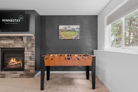 Foosball table in a cozy room with a fireplace and a view of a baseball field on the wall.