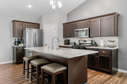Modern kitchen with granite island, dark wood cabinets, and stainless-steel appliances.