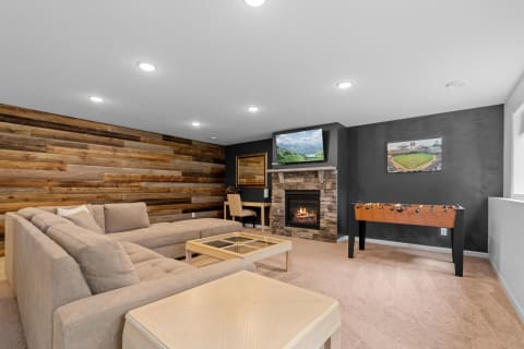 Cozy basement living room with a sectional sofa, stone fireplace, and foosball table.