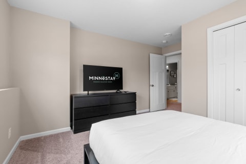 Cozy bedroom with a white bed, black dresser, and television.
