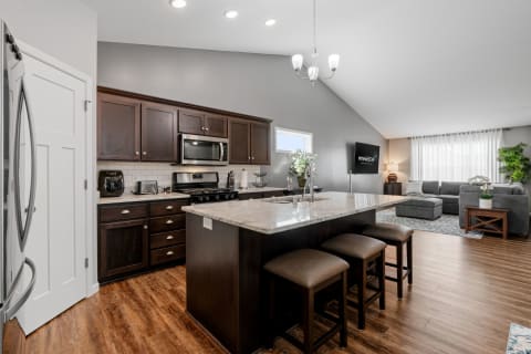 A modern kitchen with dark cabinets and a cozy living room adjacent to it.