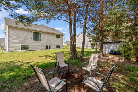 A fire pit with chairs in a backyard, surrounded by trees and houses.