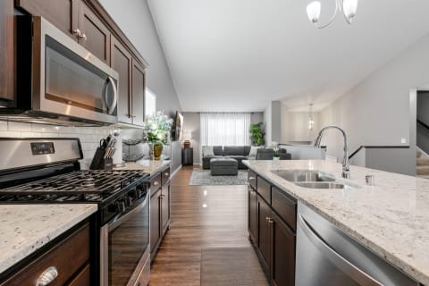 A modern kitchen with dark wood cabinets and a view of a living room with gray furniture.