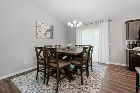 Modern dining room with a wooden table, chairs, and a chandelier under soft lighting.