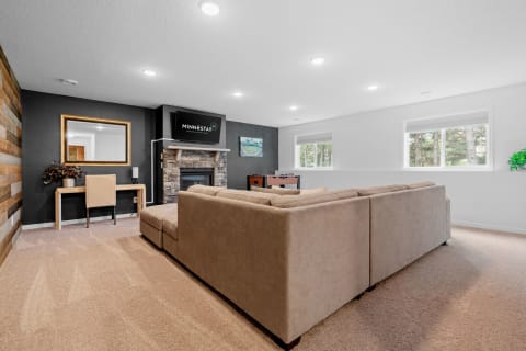 Cozy living room featuring a beige sectional sofa, stone fireplace, and natural light from windows.