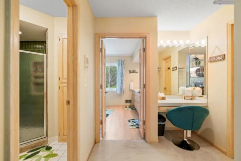 A view of a stylish bathroom featuring a glass shower, dual vanity, and teal chair.