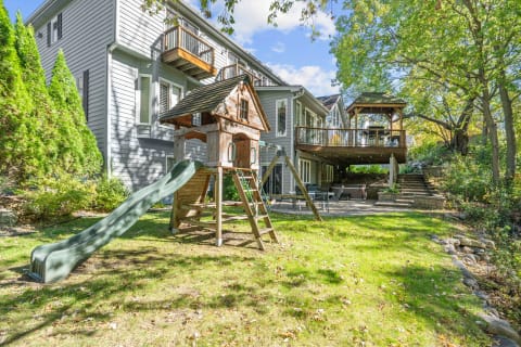 Backyard with a wooden playground and a modern house in the background.
