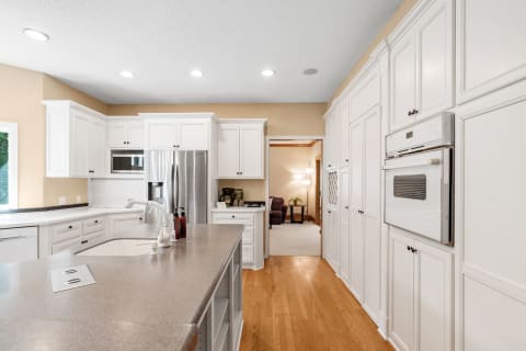Bright kitchen with white cabinets, grey countertops, and stainless steel appliances.