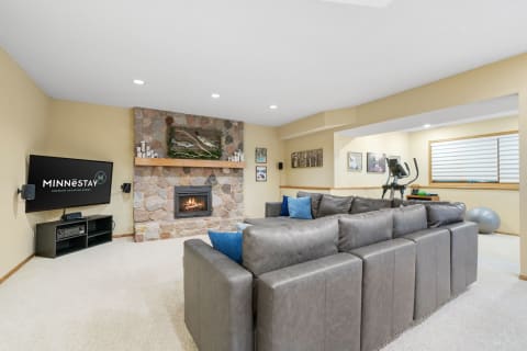 Inviting basement space featuring a sectional sofa, stone fireplace, and exercise equipment.