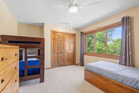 A cozy bedroom featuring a wooden bunk bed, a single bed, and a large window with a view of trees.