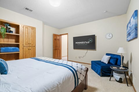 A cozy bedroom featuring a bed, decorative shelving, a wall-mounted TV, and a reading chair.