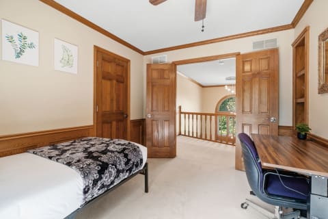 Cozy bedroom featuring a bed, desk, and wooden details with botanical artwork.