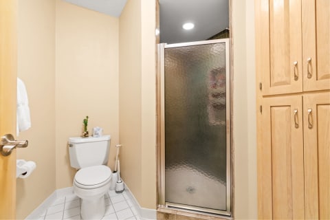 A compact bathroom with a white toilet, glass shower, and wooden cabinets.