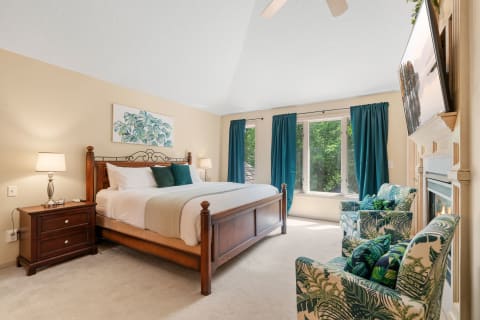 A warm and inviting bedroom featuring a wooden bed, teal curtains, and tropical-themed chairs.