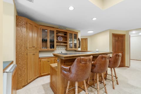 Cozy home bar with leather stools and wooden cabinets.