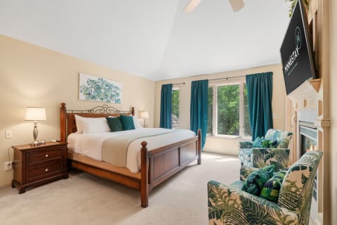 Cozy bedroom with wooden bed, fireplace, and green chairs.