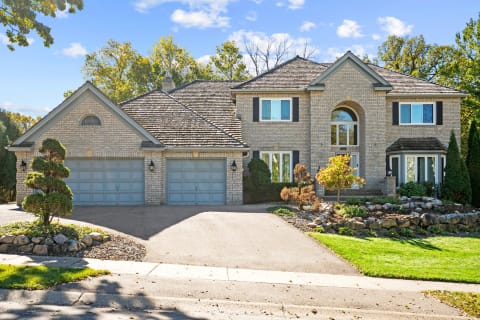 Large two-story gray brick house with blue garage doors and landscaped front yard.