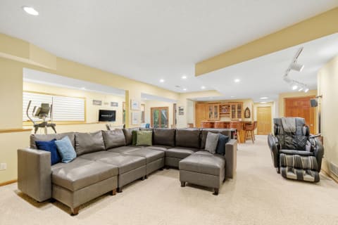 Spacious basement with sectional sofa, fitness machine, and bar area.
