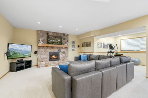 A well-decorated basement living room featuring a sectional sofa, a stone fireplace, and a contemporary TV.