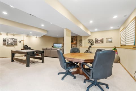 A spacious basement with a couch, air hockey table, dartboard, and exercise bike, showcasing a welcoming recreational space.