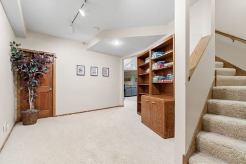 A warm and inviting basement space with carpet, a bookshelf filled with games, and framed bird pictures on the wall.