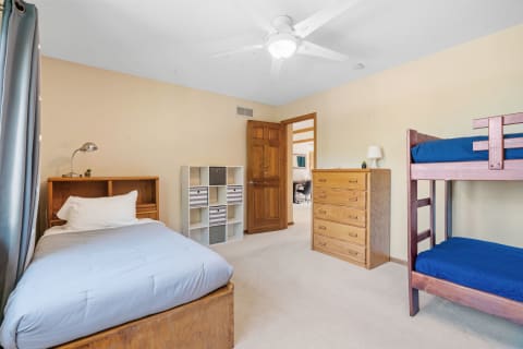 A tidy bedroom with a single bed, bunk bed, wooden dresser, and storage shelves.
