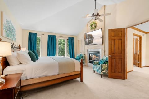 A stylish bedroom with a king-sized bed, teal curtains, and tropical flower patterned chairs.