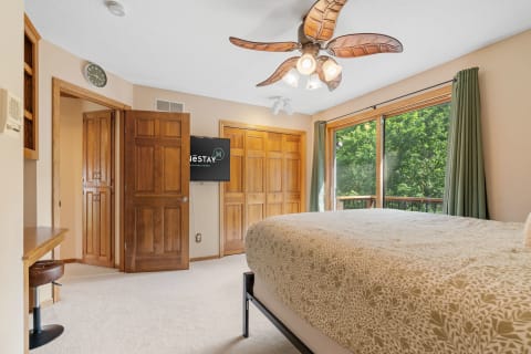 Cozy bedroom with a bed, wooden furniture, and a large window overlooking trees.