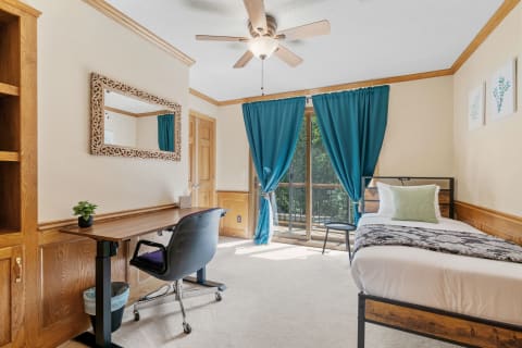 Cozy bedroom with a bed, desk, and large window with turquoise curtains.