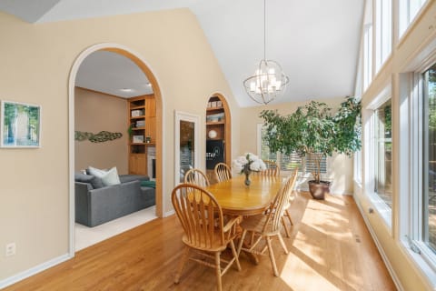 A spacious dining area featuring a wooden table, modern chandelier, and a view of a living room with a gray sofa.