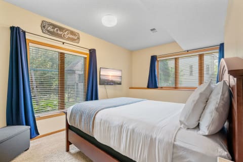 Cozy guest bedroom featuring a bed with blue throw, navy curtains, and a mounted TV.