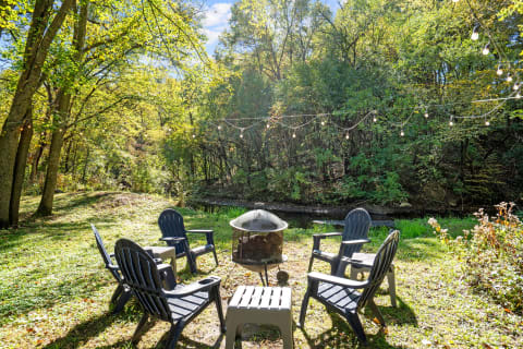 Inviting outdoor space with a fire pit and Adirondack chairs amidst greenery.