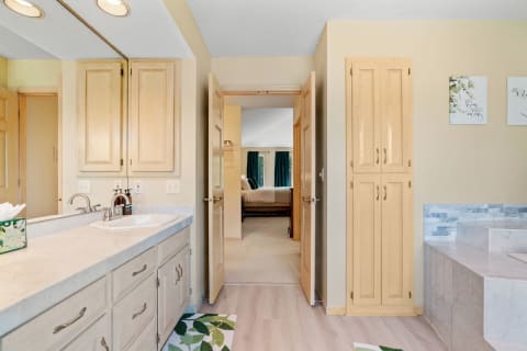 Interior view of a modern bathroom featuring dual sinks, wooden cabinetry, and an adjacent bedroom.