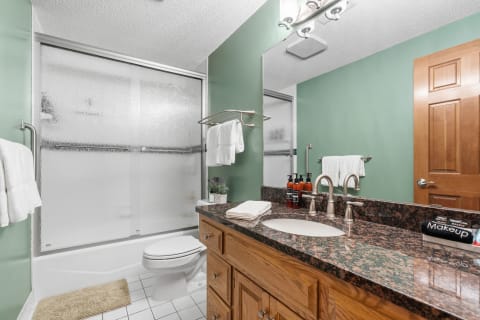 Modern bathroom with a green wall and granite countertop, including a shower and neatly arranged towels.