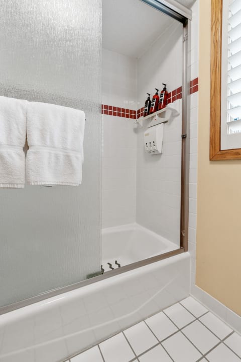 Clean shower area with glass door, white tiles, red accents, and toiletries.