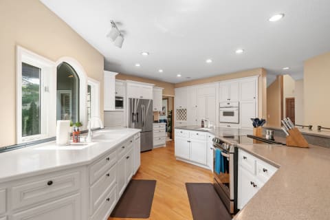 A modern kitchen with white cabinets, stainless steel appliances, and wooden flooring.