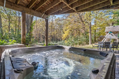 An outdoor hot tub with steam, surrounded by colorful autumn trees and shaded by a wooden pergola.