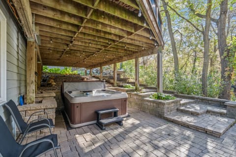 Outdoor space with a hot tub and seating area under a wooden structure.