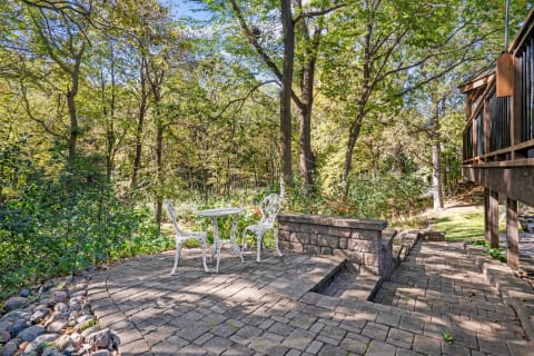 A white table and chairs on a stone patio, surrounded by trees and greenery.