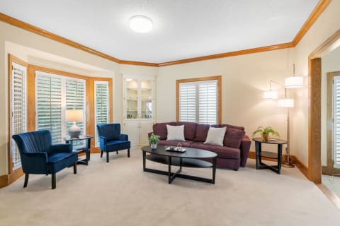 A stylish living room with a purple couch, blue chairs, and natural light from shutters.