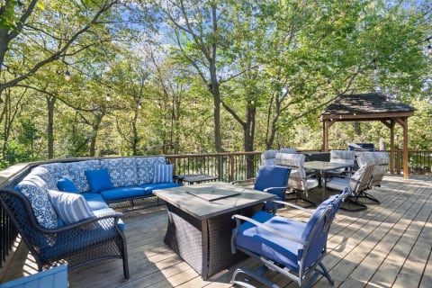 An inviting outdoor space featuring a blue sectional sofa and several chairs on a wooden deck, surrounded by trees and a gazebo.