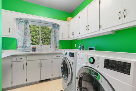 Bright green laundry room featuring modern washing machines and patterned curtains.