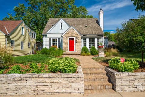 A picturesque home with a red front door and stone accents, set in a lush garden.