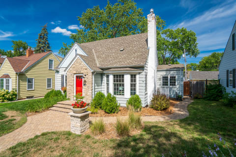 A quaint house with a red door and landscaped front yard under a blue sky.