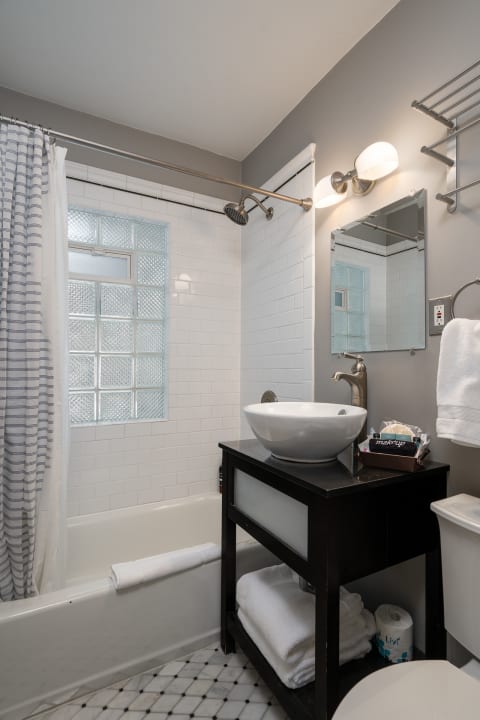 Modern bathroom featuring a round vessel sink, a shower area with a glass block window, and patterned tile floor.