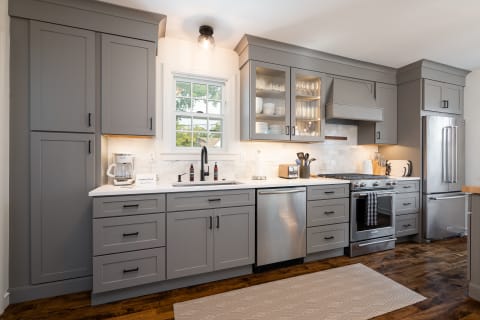 Modern kitchen featuring gray cabinets, white countertops, and stainless-steel appliances under natural light.